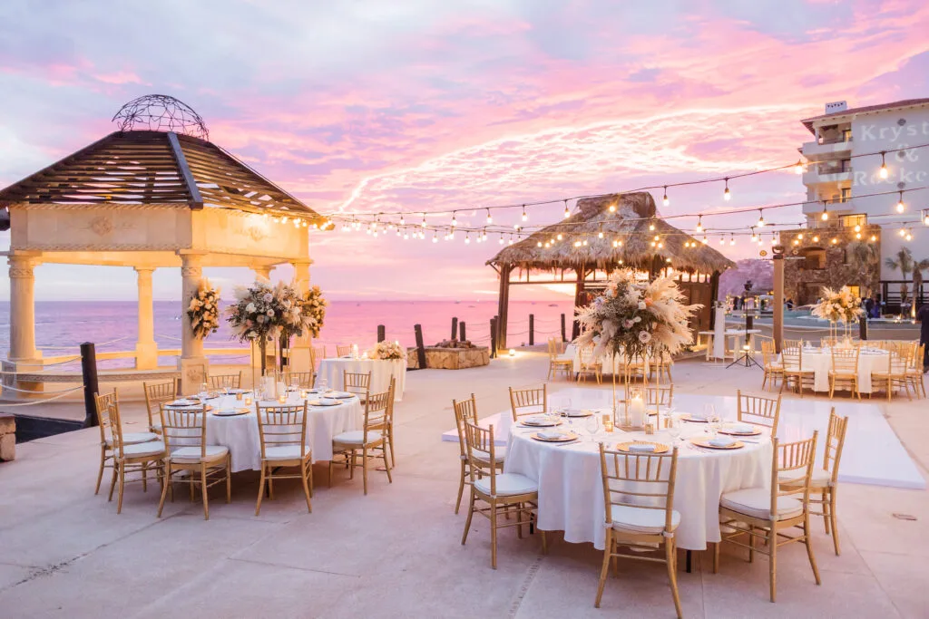 Gold-chair reception tables set on a terrace under a pink sunset sky