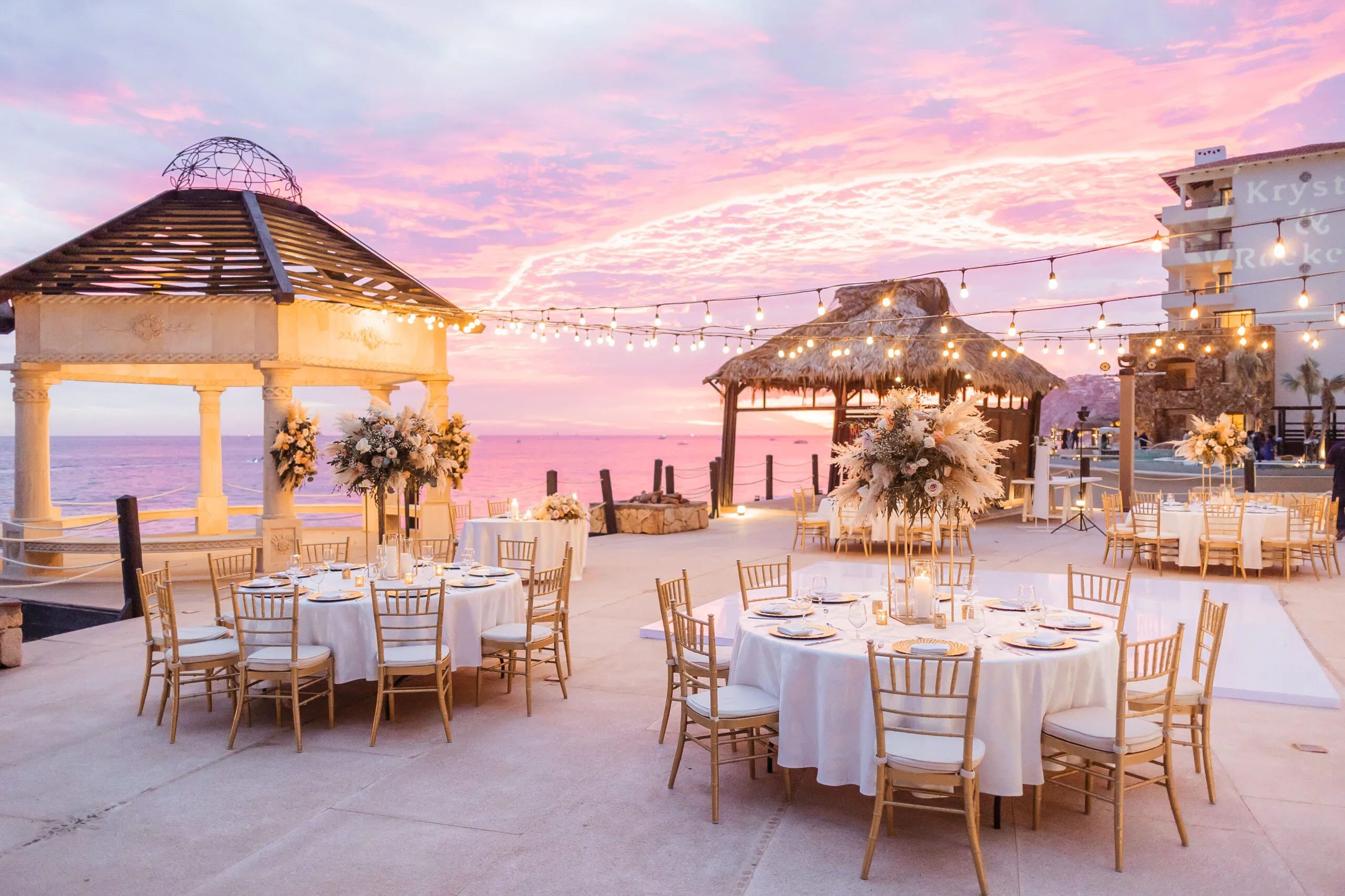 Gold-chair reception tables set on a terrace under a pink sunset sky