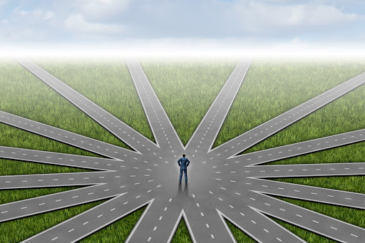 A person standing at a crossroads with multiple paths, representing the choice points where tiny experiments can guide decisions