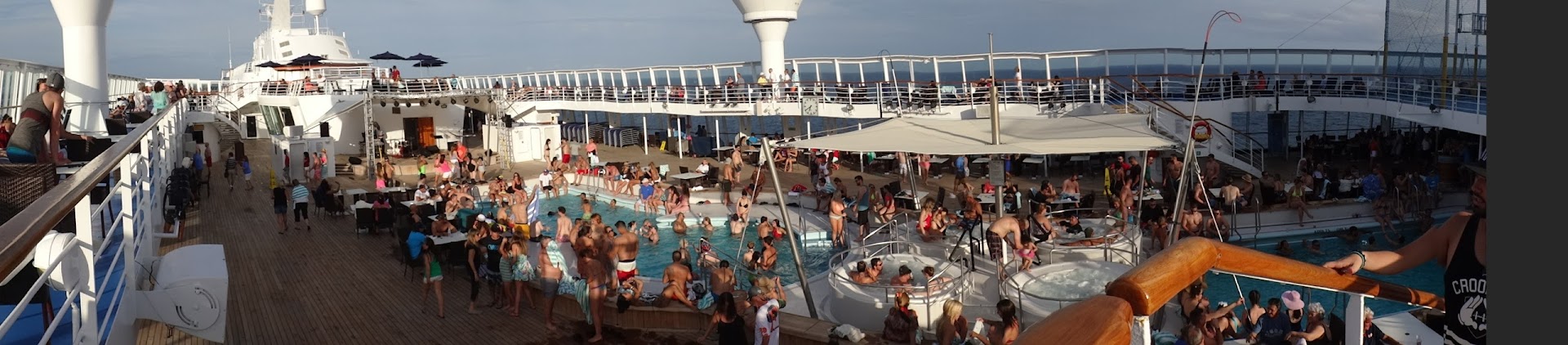 Panorama of the crowded cruise ship pool deck packed with sunbathers