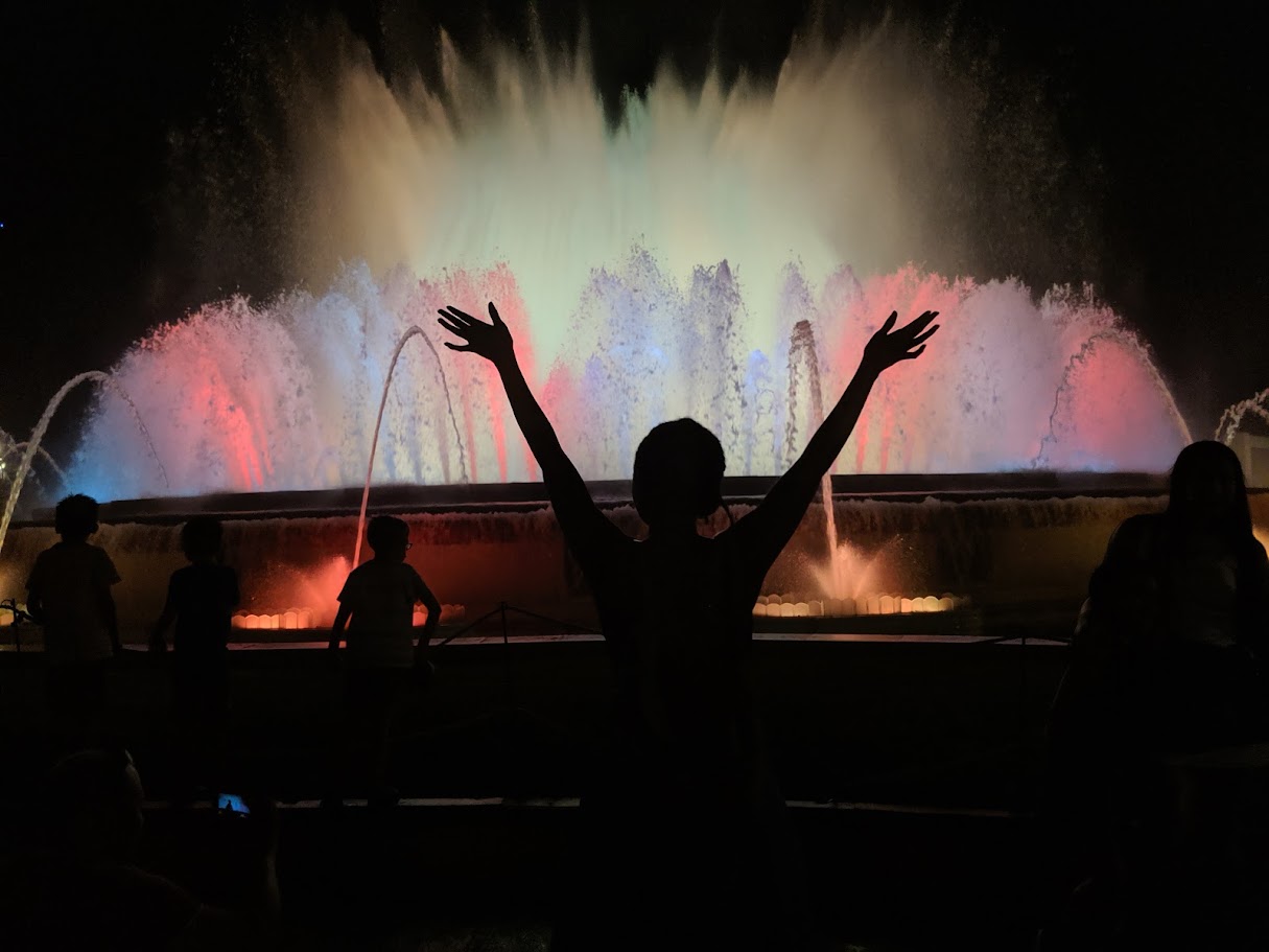 Silhouette with arms raised before the colorfully lit Magic Fountain of Montjuic in Barcelona