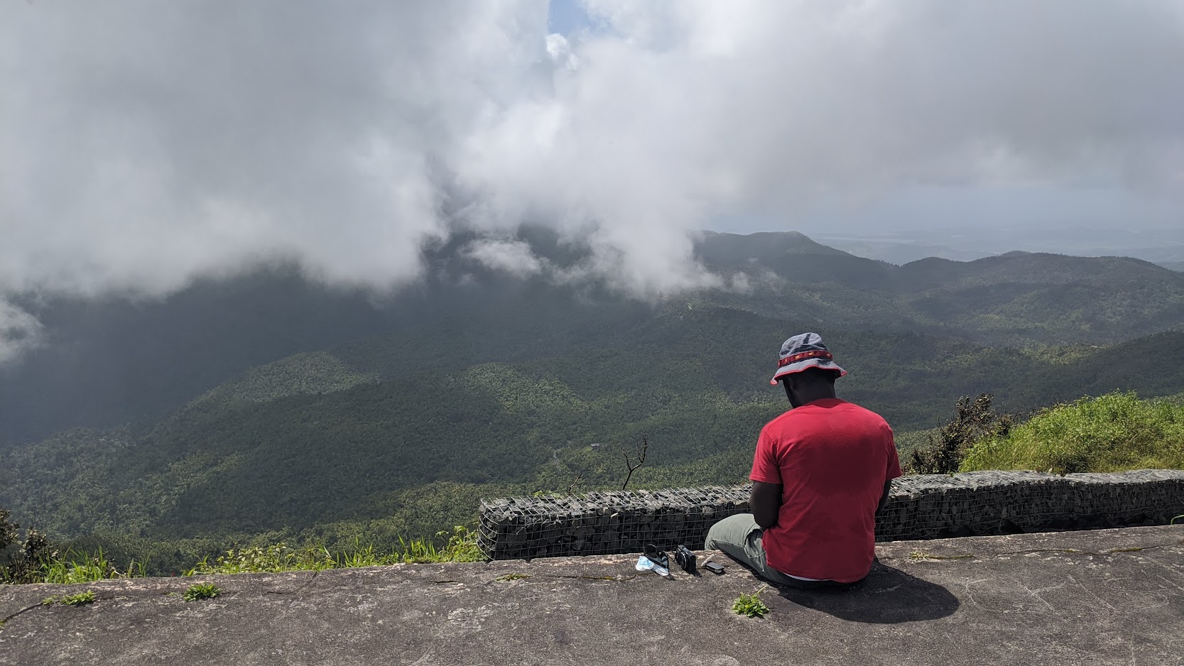 Person seated on a wall overlooking the misty green mountains of El Yunque