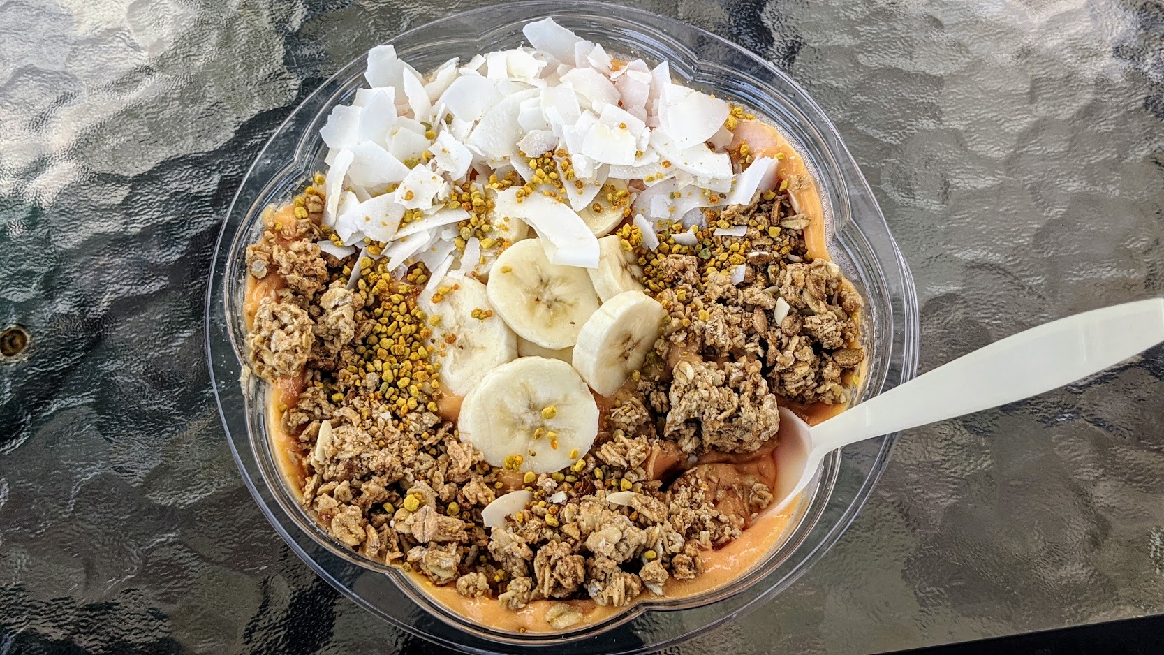 Smoothie bowl topped with sliced banana, granola, coconut flakes and bee pollen