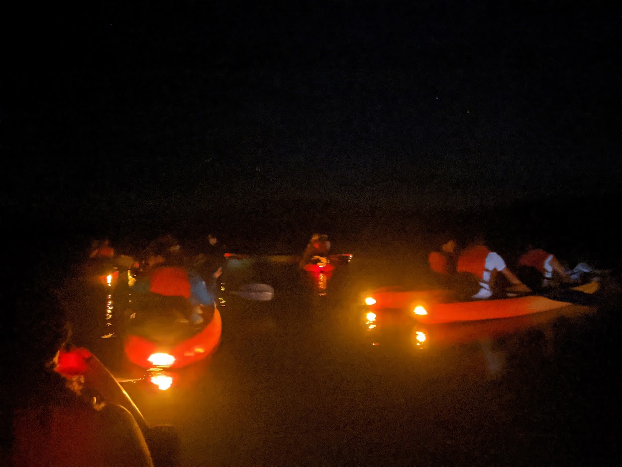 Cluster of lit kayaks reflecting on dark water during the night canal tour