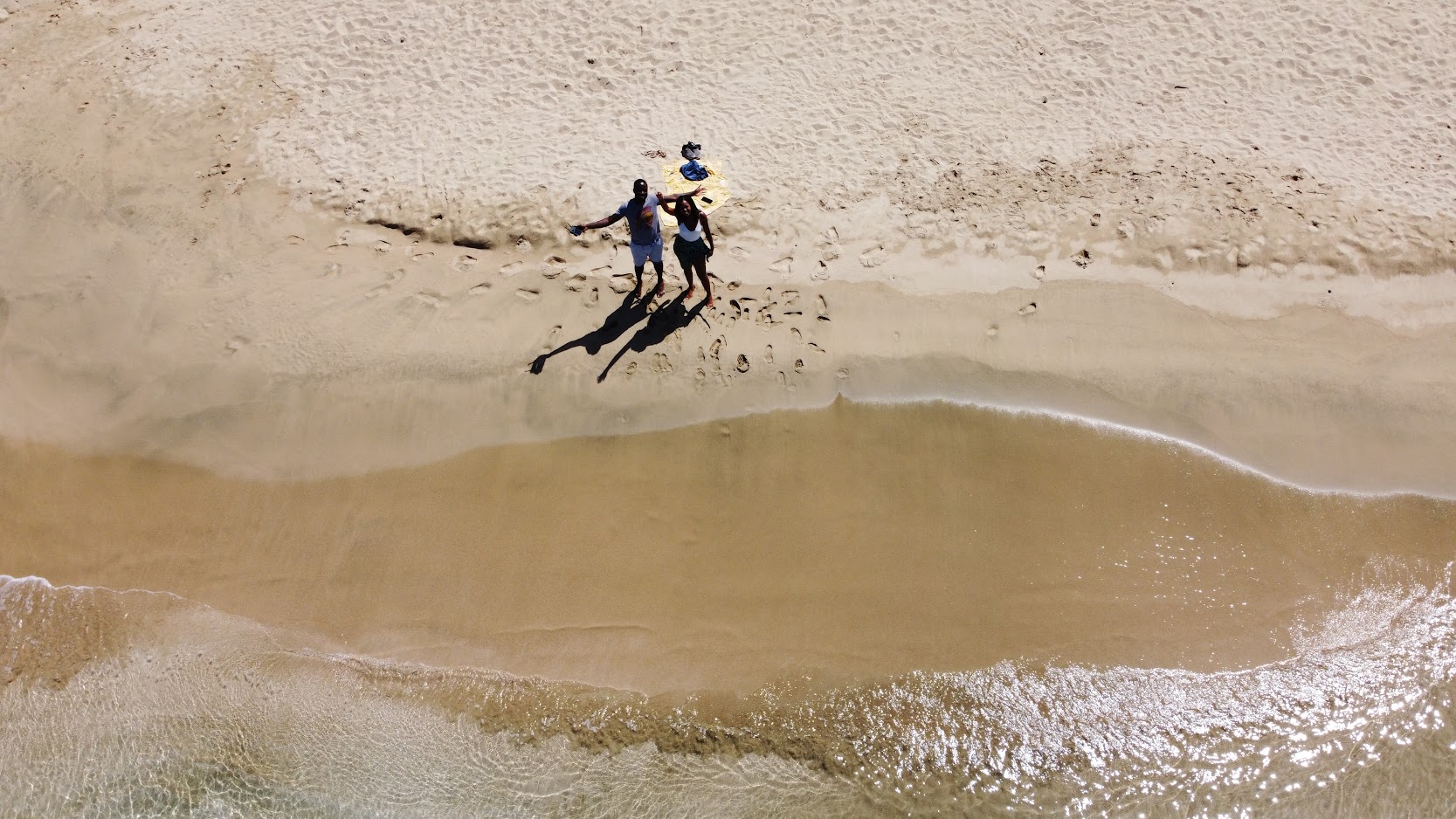 Overhead drone view of a couple posing on the sand beside lapping waves