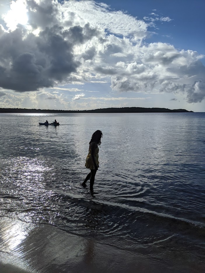 Woman in a yellow dress wading at the shore under dramatic cloudy skies