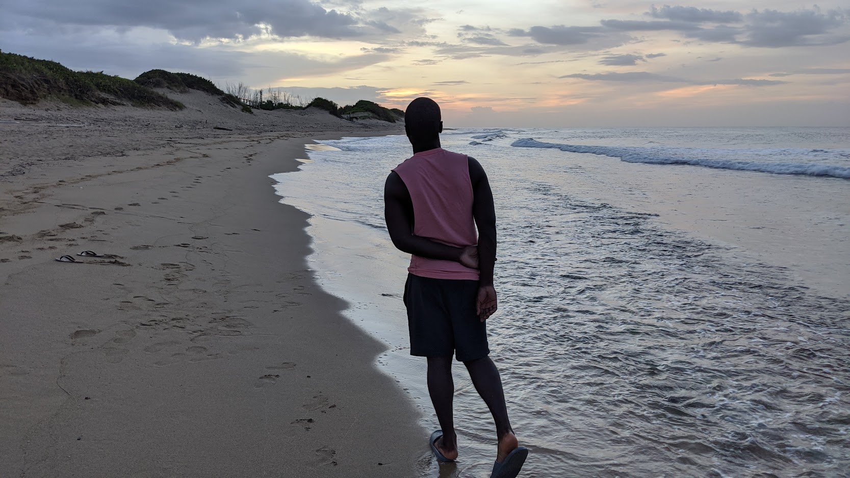 Man looking out over the surf along an empty beach at sunset