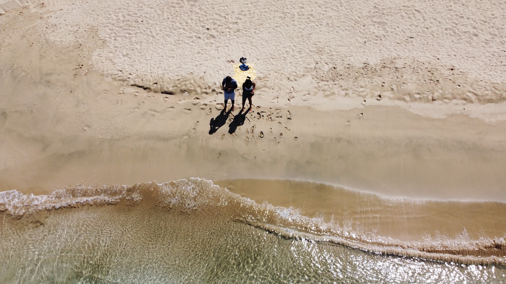 Overhead drone view of three people on the sand where waves meet the beach
