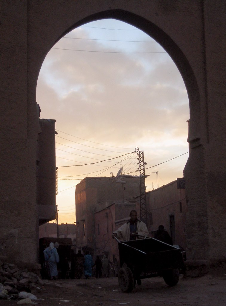 A street scene in the Marrakech medina at sunset, a man with a cart framed by a Moorish arch